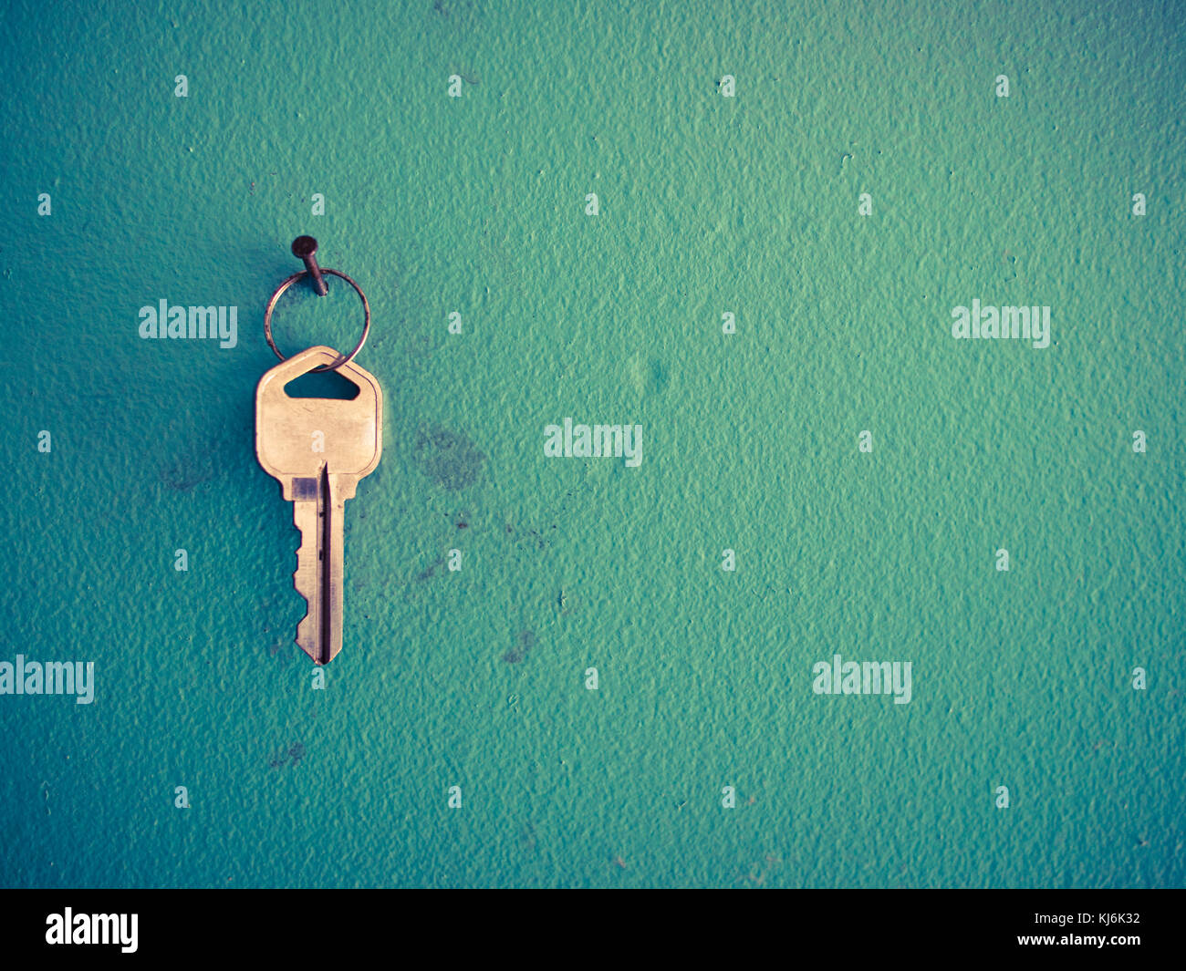 A silver key hanging on a nail on a green wall with fingerprints Stock
