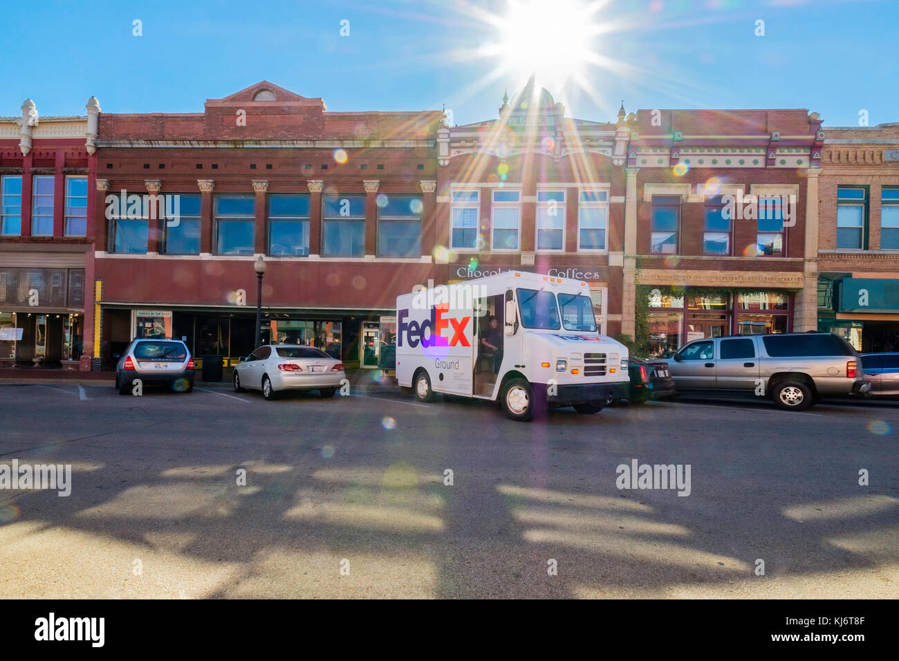 A FedEx delivery truck delivering goods to Guthrie historic district in Guthrie, Oklahoma, USA. Strong sun flare that emphasizes the FedEx truck. Stock Photo