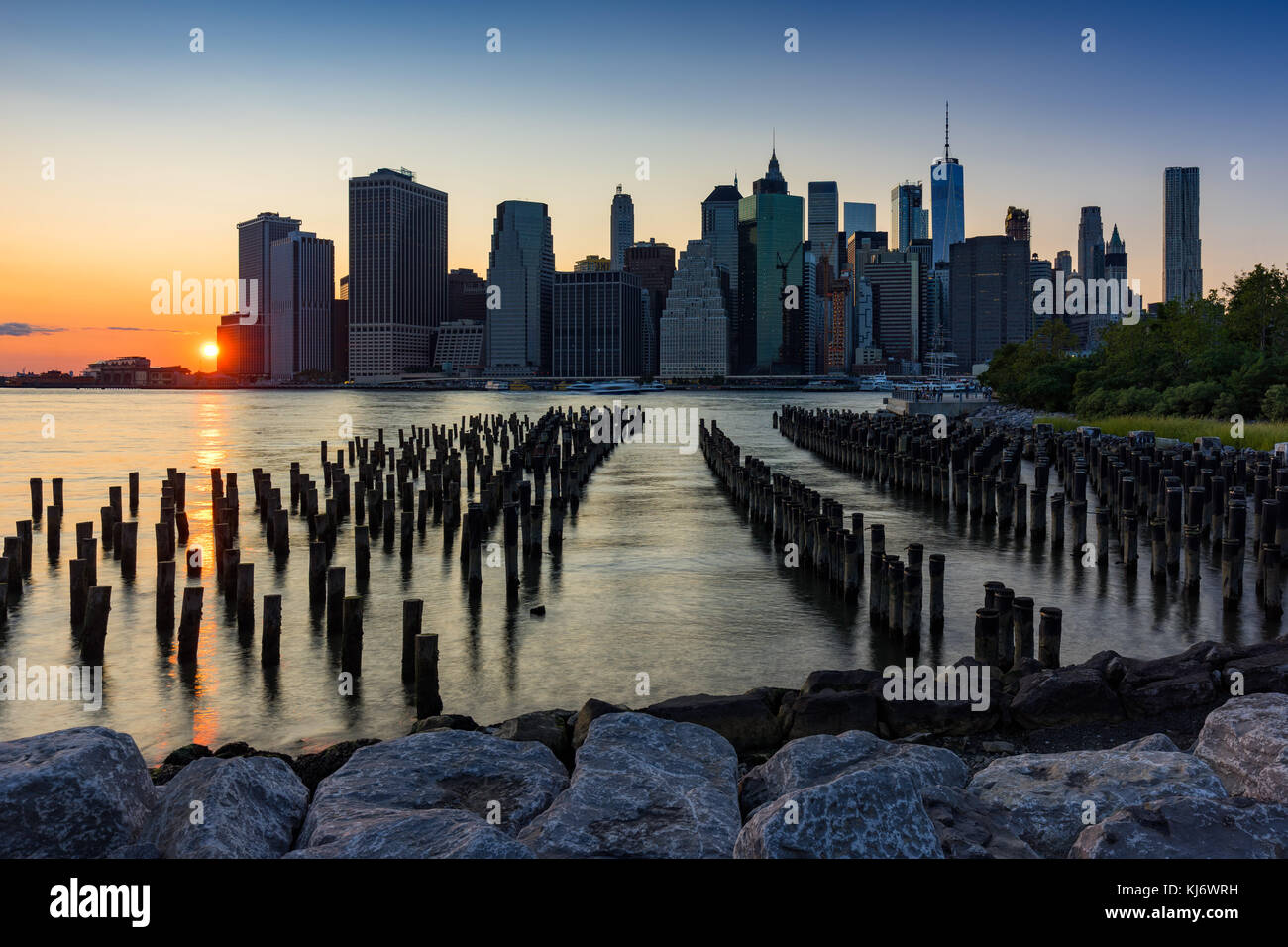 Skyscrapers of Lower Manhattan and wood pilings at Sunset from Brooklyn Bridge Park. Manhattan, New York City Stock Photo