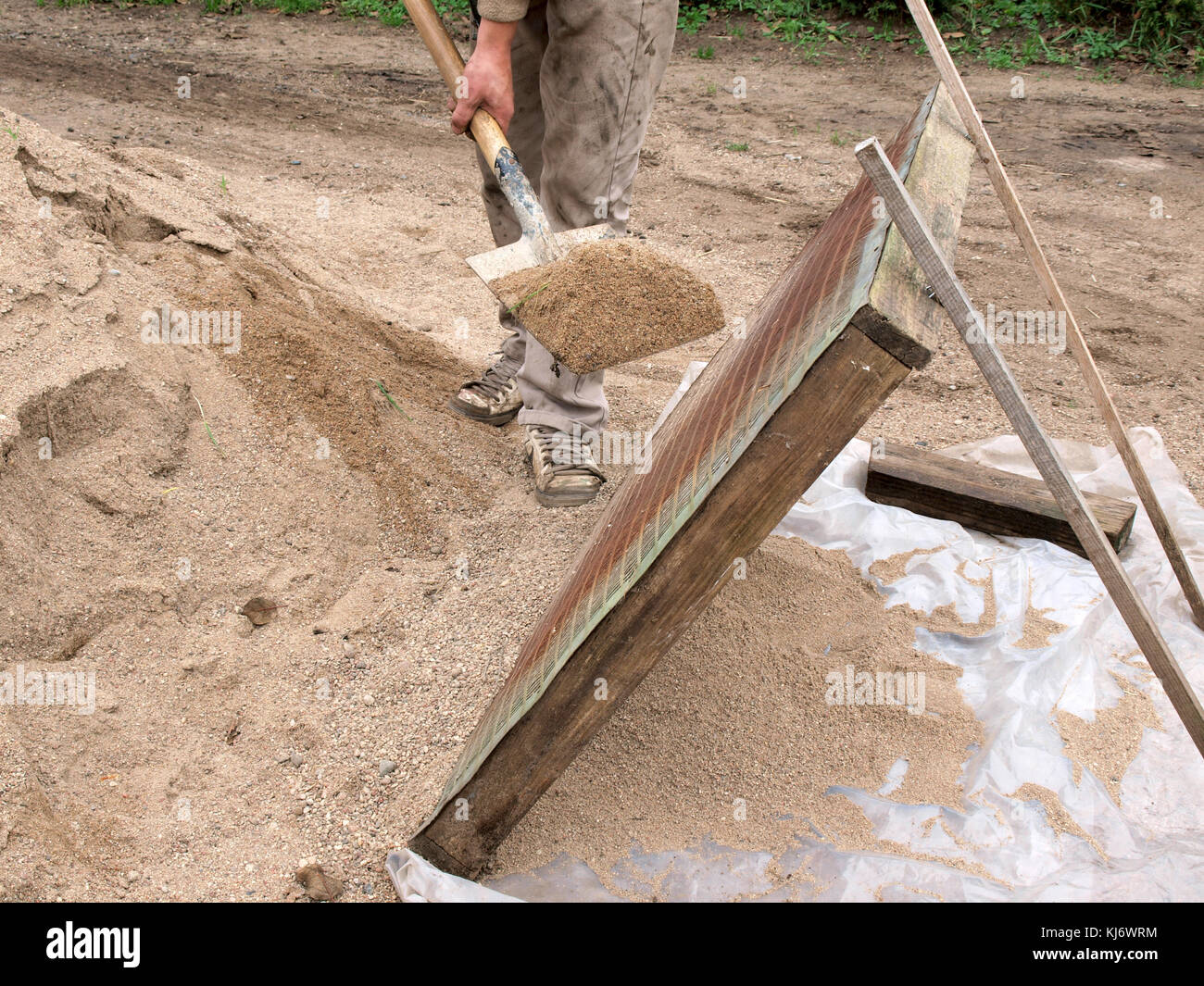 Construction worker sifting gravel through a sieve with shovel Stock