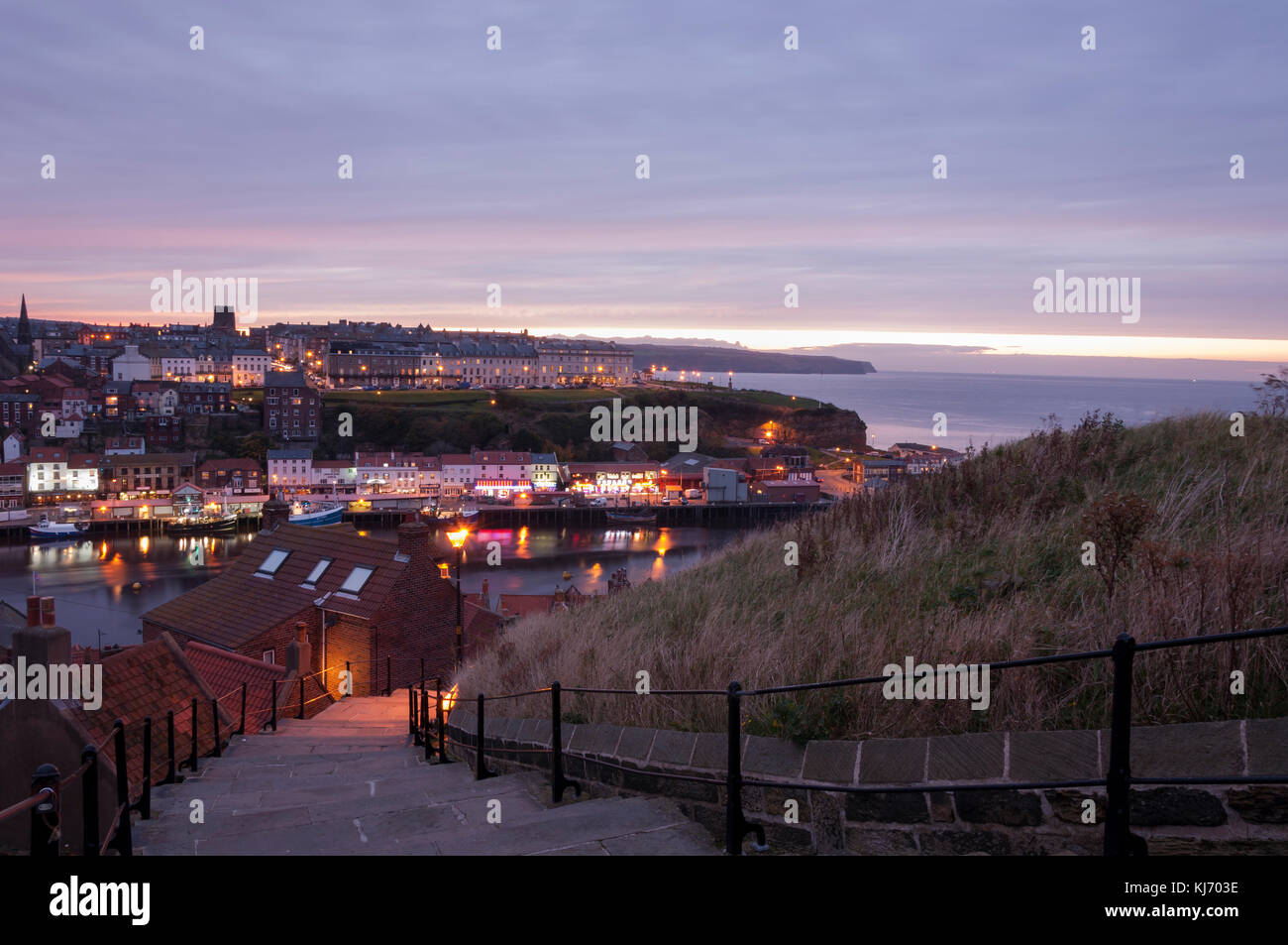 View of the coastal town of Whitby in North Yorkshire at dusk, looking towards the harbor mouth from the 199 steps, on an October evening in October. Stock Photo