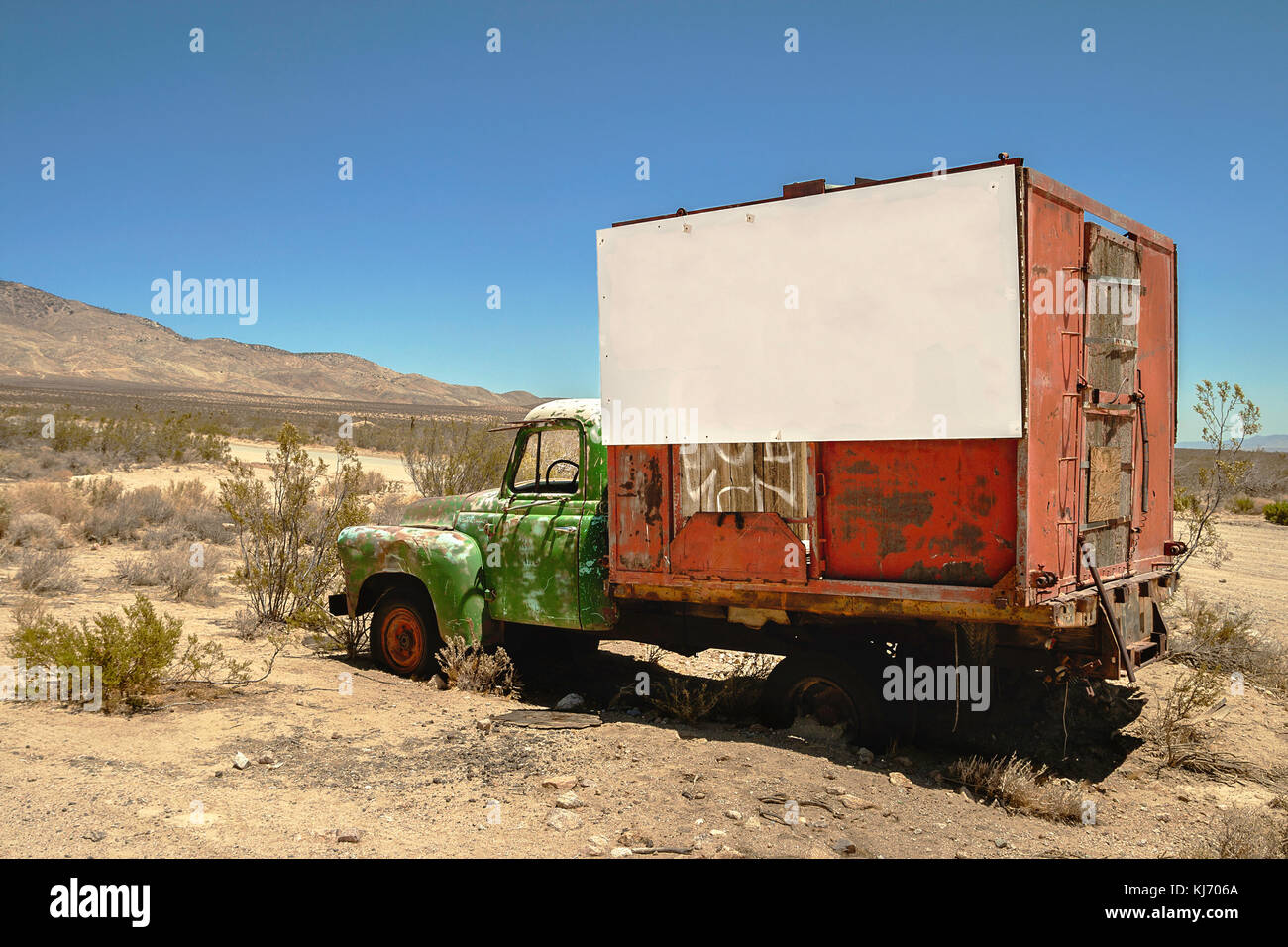 A wreckage of a red and green truck with a white large signboard in the desert. Stock Photo