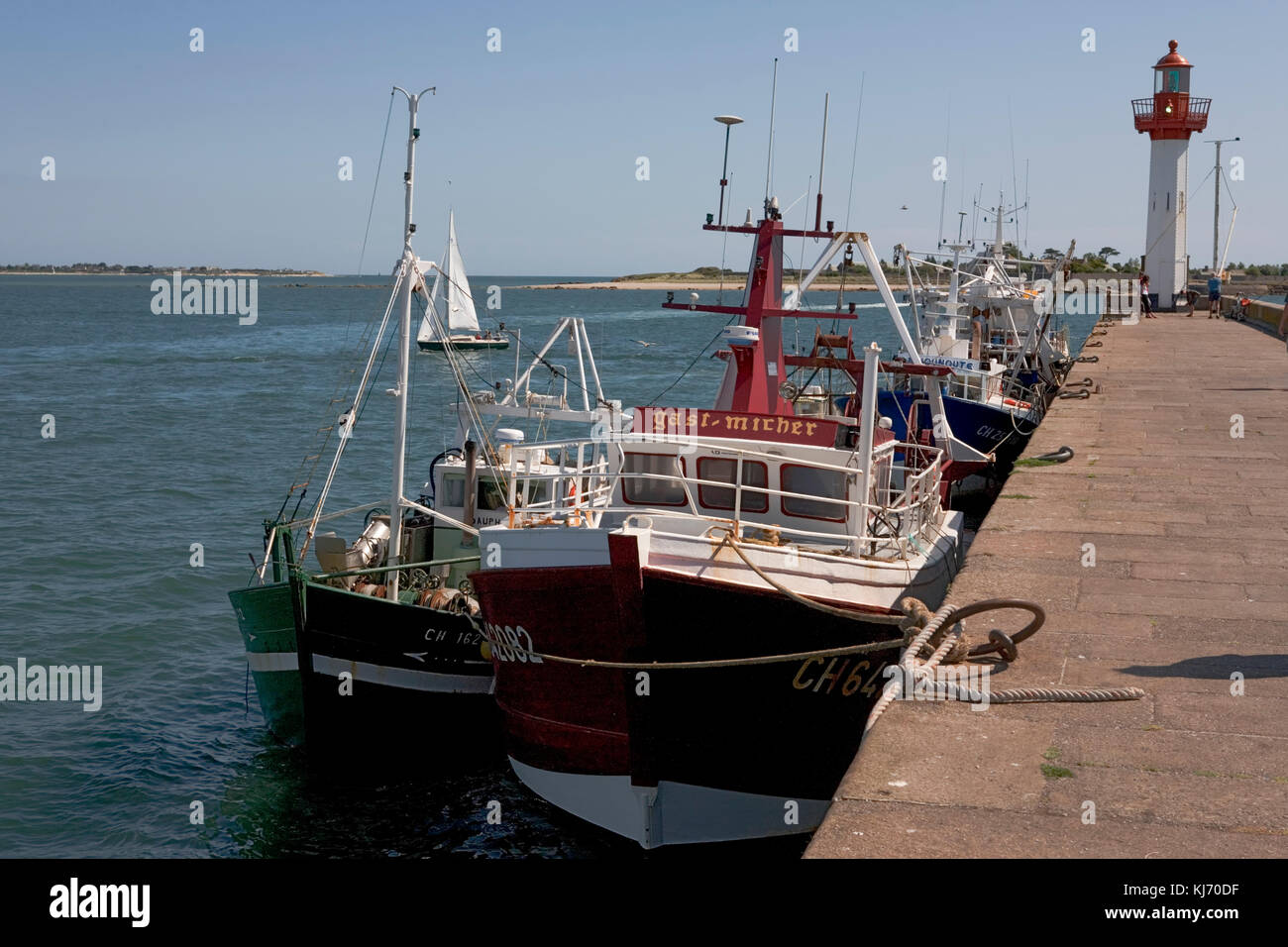 St Vaast harbour breakwater, with lighthouse and moored fishing boats alongside, Normandy, France Stock Photo