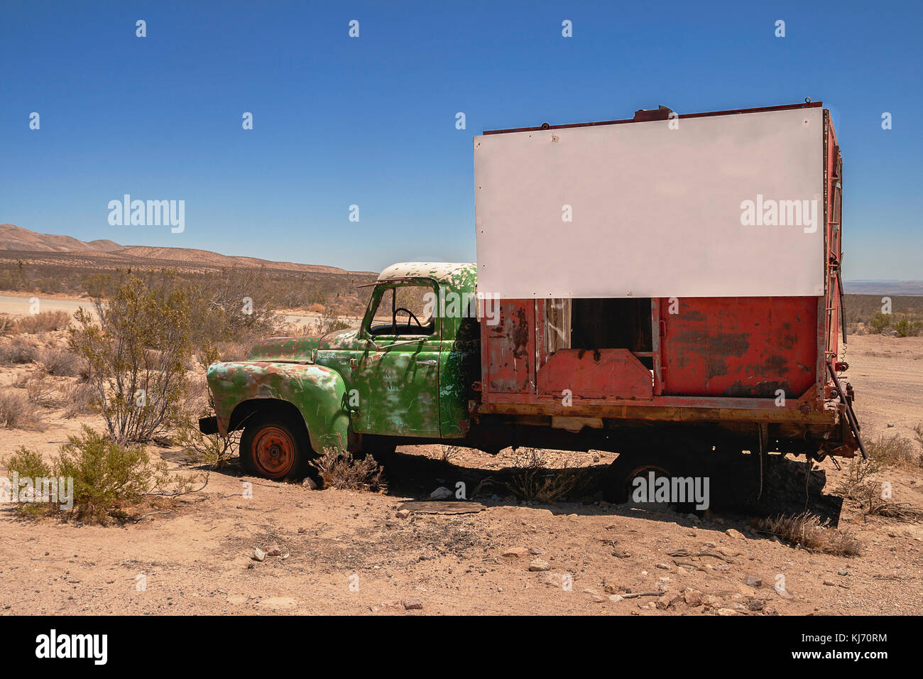 A wreckage of a red and green truck with a white large signboard in the desert. Stock Photo