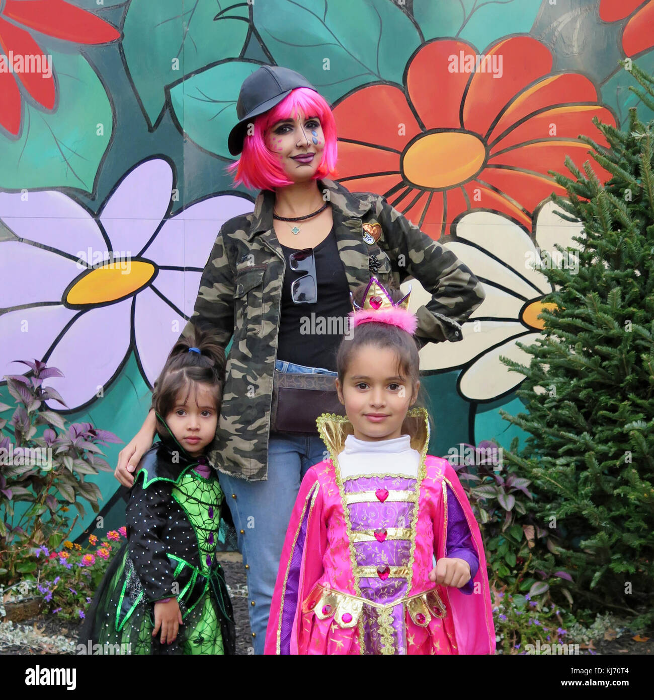 portrait of a Mother and two daughters in Halloween costumes going trick or treating. Daughters wearing a fairy costume and witch costume. Stock Photo