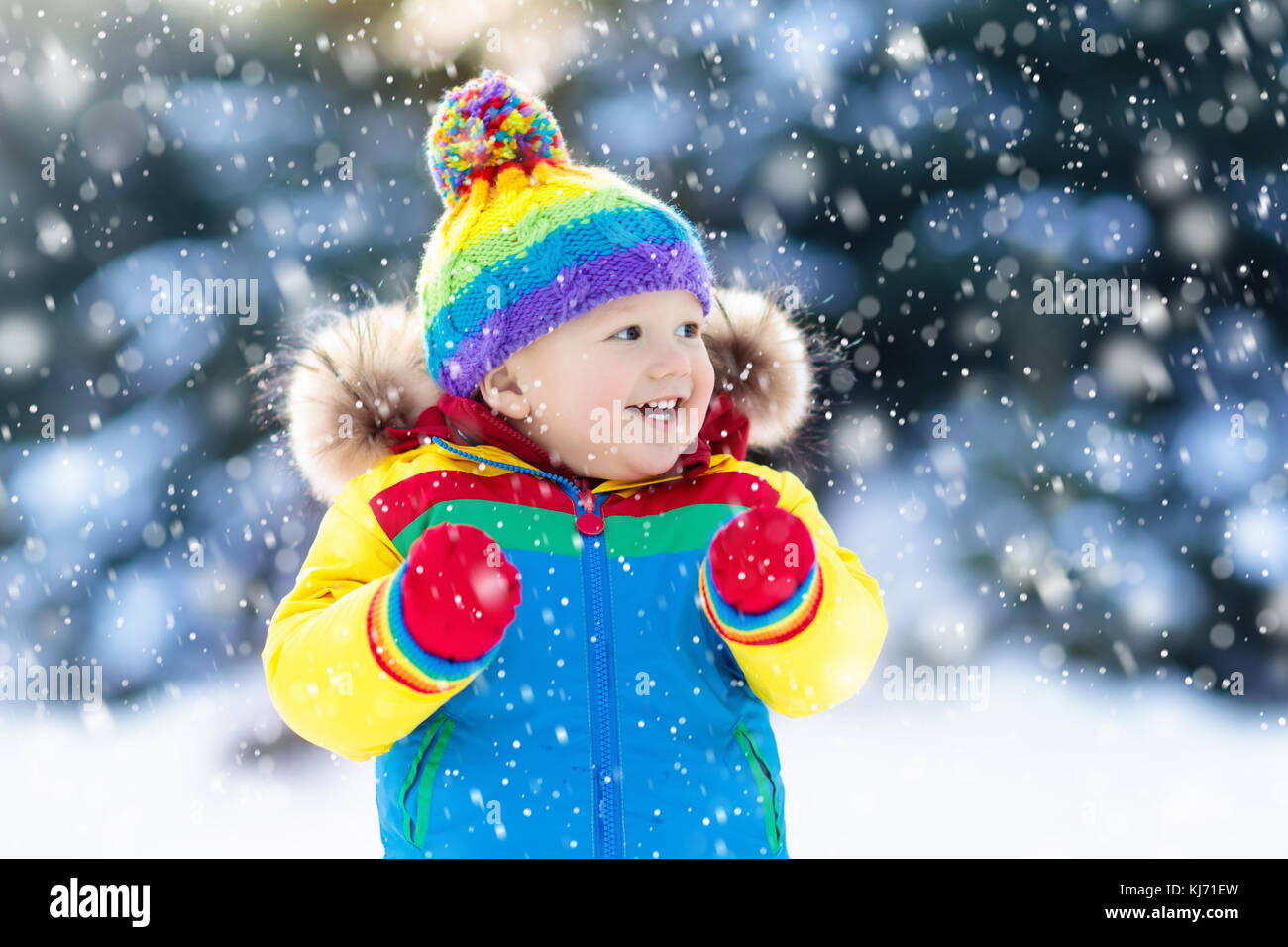 Child playing with snow in winter. Little boy in colorful jacket and ...