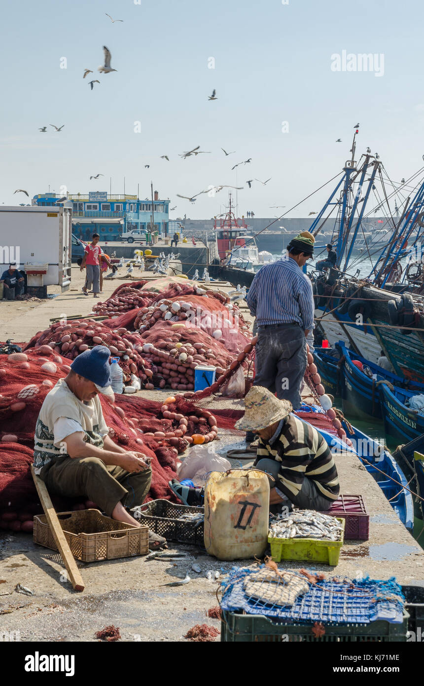 Essaouira, Morocco - September 15 2013: Unidentified local fishermen fixing nets at harbor with seagulls and boats Stock Photo
