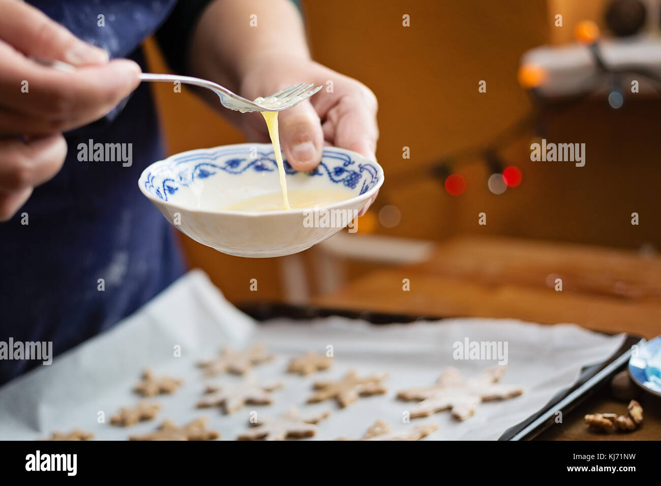 Woman checking the consistency of the mixed egg. She is holding a small bowl, and mixing an egg with a fork. Focus on hands. Baking at home for Christ Stock Photo