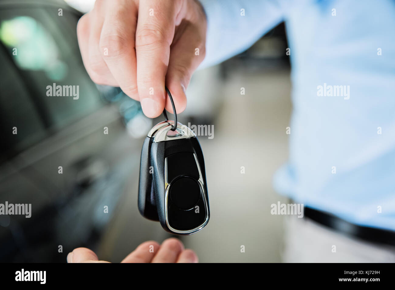 close up photo of male hand giving car keys to female hand, indoors in car dealership Stock Photo