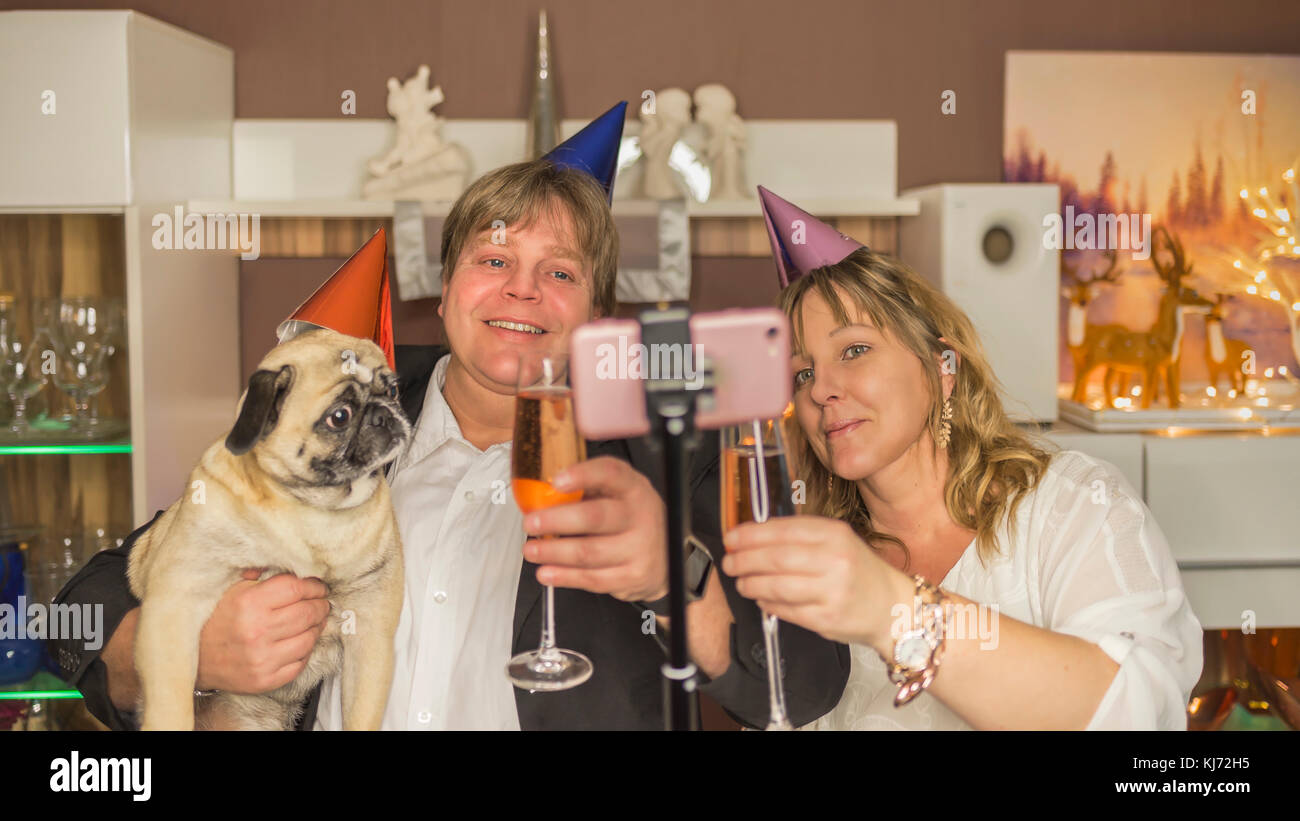 Middle aged couple makes with their pug a selfie during a New Year's Eve party at home Stock Photo