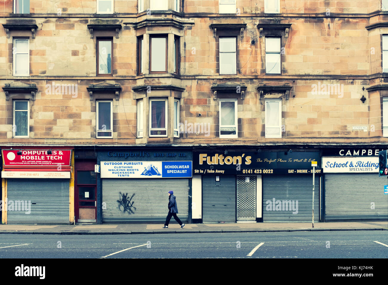 Closed shops with shutters down below tenement apartments on Victoria Road in Govanhill district of Glasgow, Scotland, United Kingdom Stock Photo