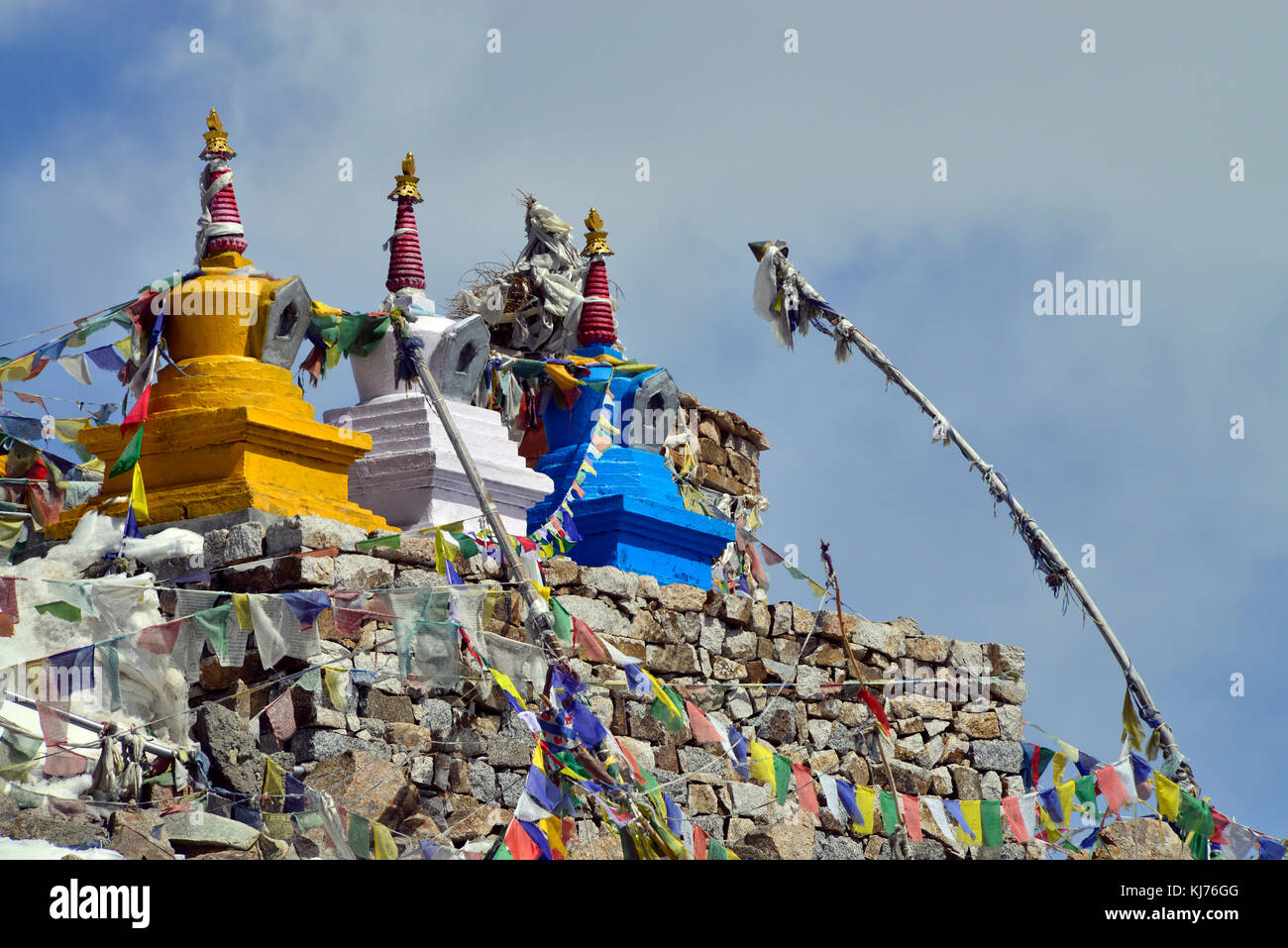 Three Buddhist stupas: yellow, white and blue at the top of masonry, hung with colored Tibetan prayer flags. Stock Photo