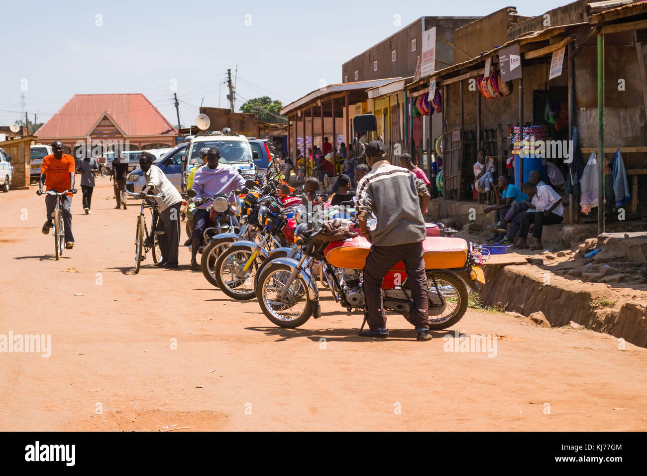 Several boda boda motorbike taxis lined up parked on a dusty road with people walking around in a town, Busia, Uganda, East Africa Stock Photo