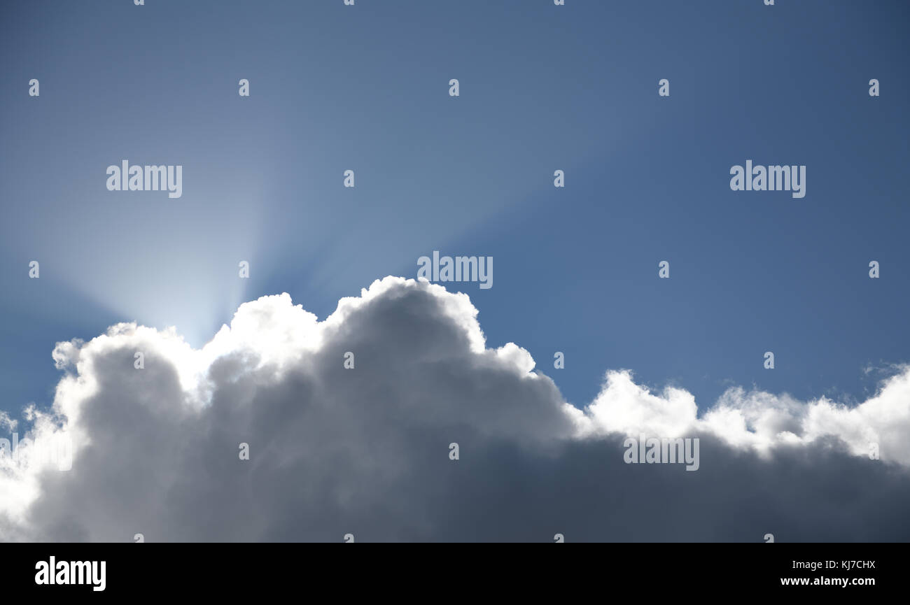 sun rays shining from behind a thick cloud on clear blue sky Stock Photo