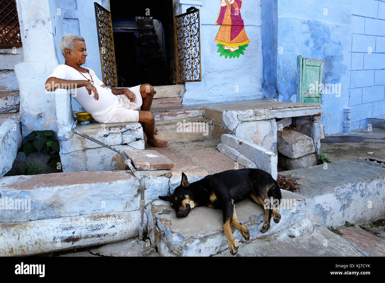 Old indian man dressed in white sitting on the stairs with his dog in front of his house, Jodhpur, Rajasthan, India. Stock Photo