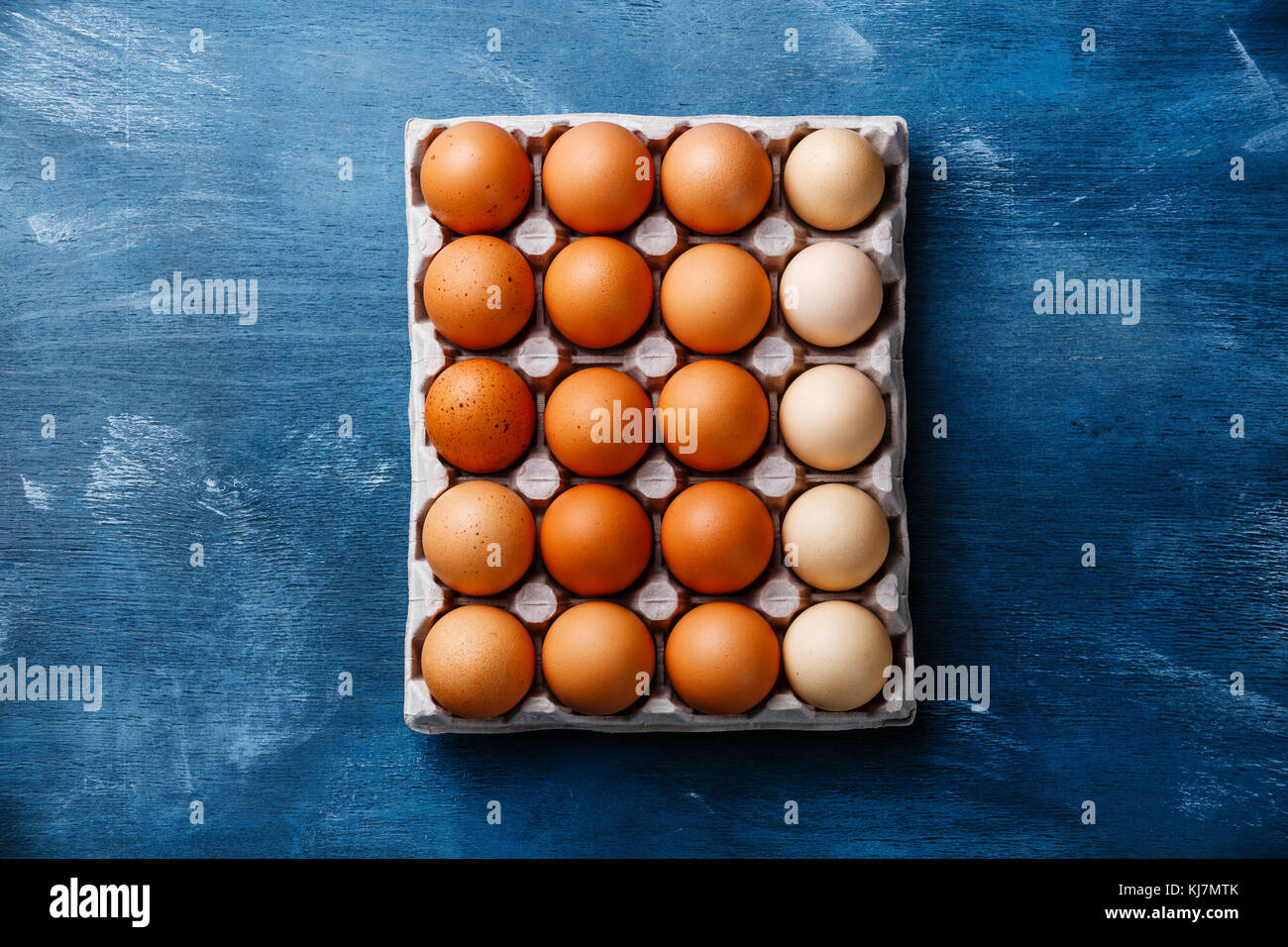 Fresh brown and speckled chicken Eggs in eco cardboard paper tray container on blue wooden background Stock Photo