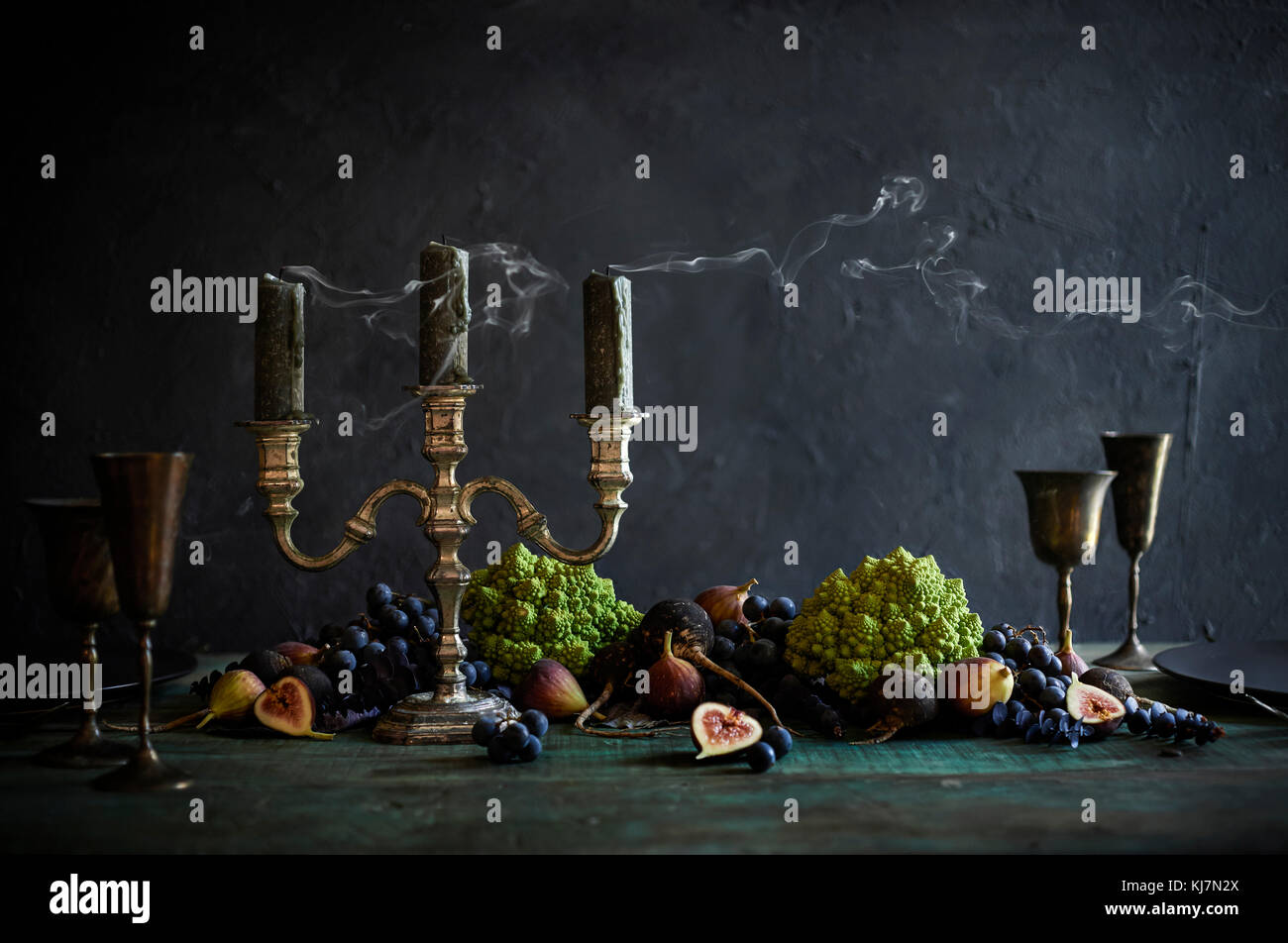 A gorgeous, creepy halloween tablescape with rustic candelabra with blown out candles. Vegetable spread across table with romanesco broccoli, concord Stock Photo