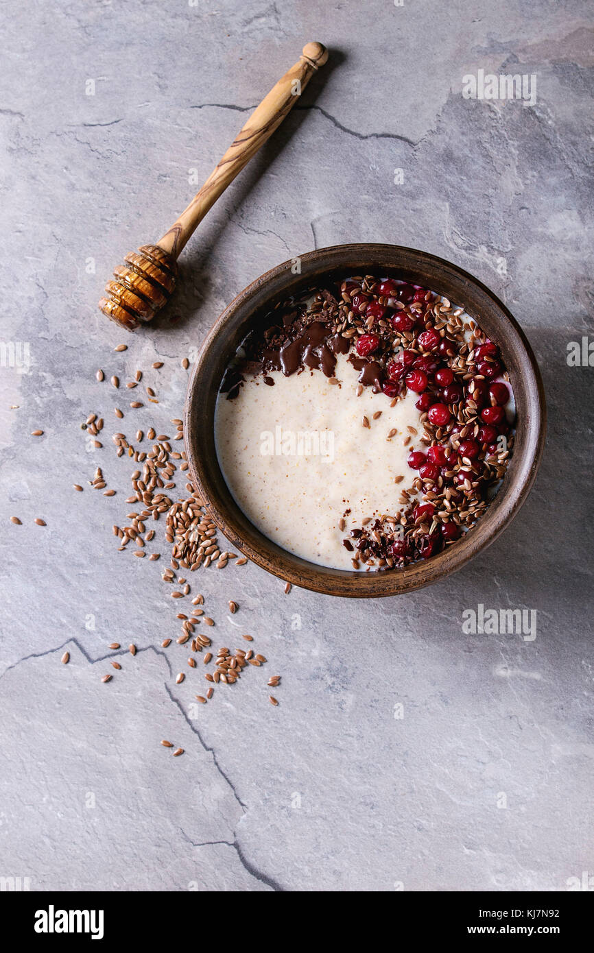 Bowl of milk cereal porridge with additives flax seeds, chocolate and berries over gray kitchen table. Top view with space Stock Photo