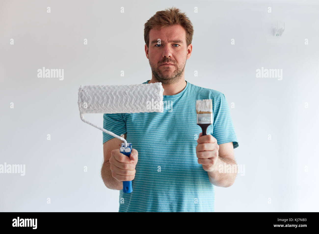 Smiling man holding a brush and a roller in front of him Stock Photo
