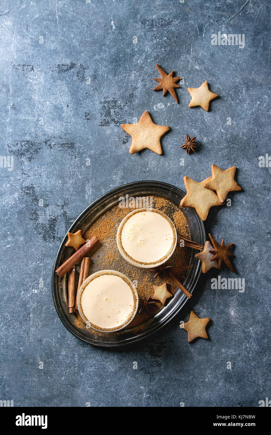 Eggnog Christmas milk cocktail with cinnamon, served in two glasses on vintage tray with shortbread star shape sugar cookies different size over blue Stock Photo