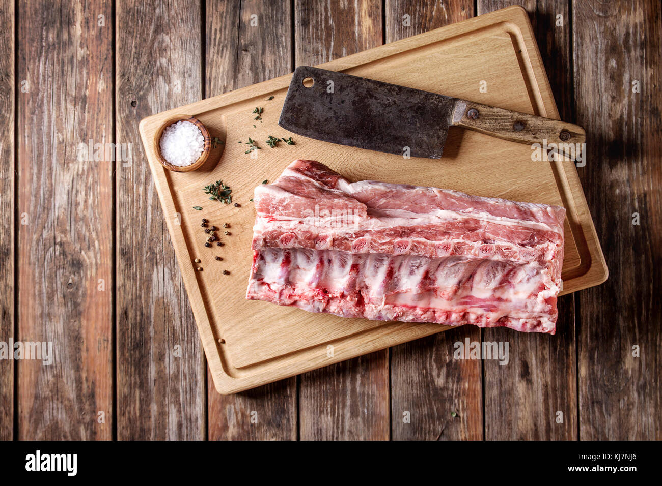 Fresh raw uncooked whole rack of pork loin with ribs on wooden cutting board with salt, thyme