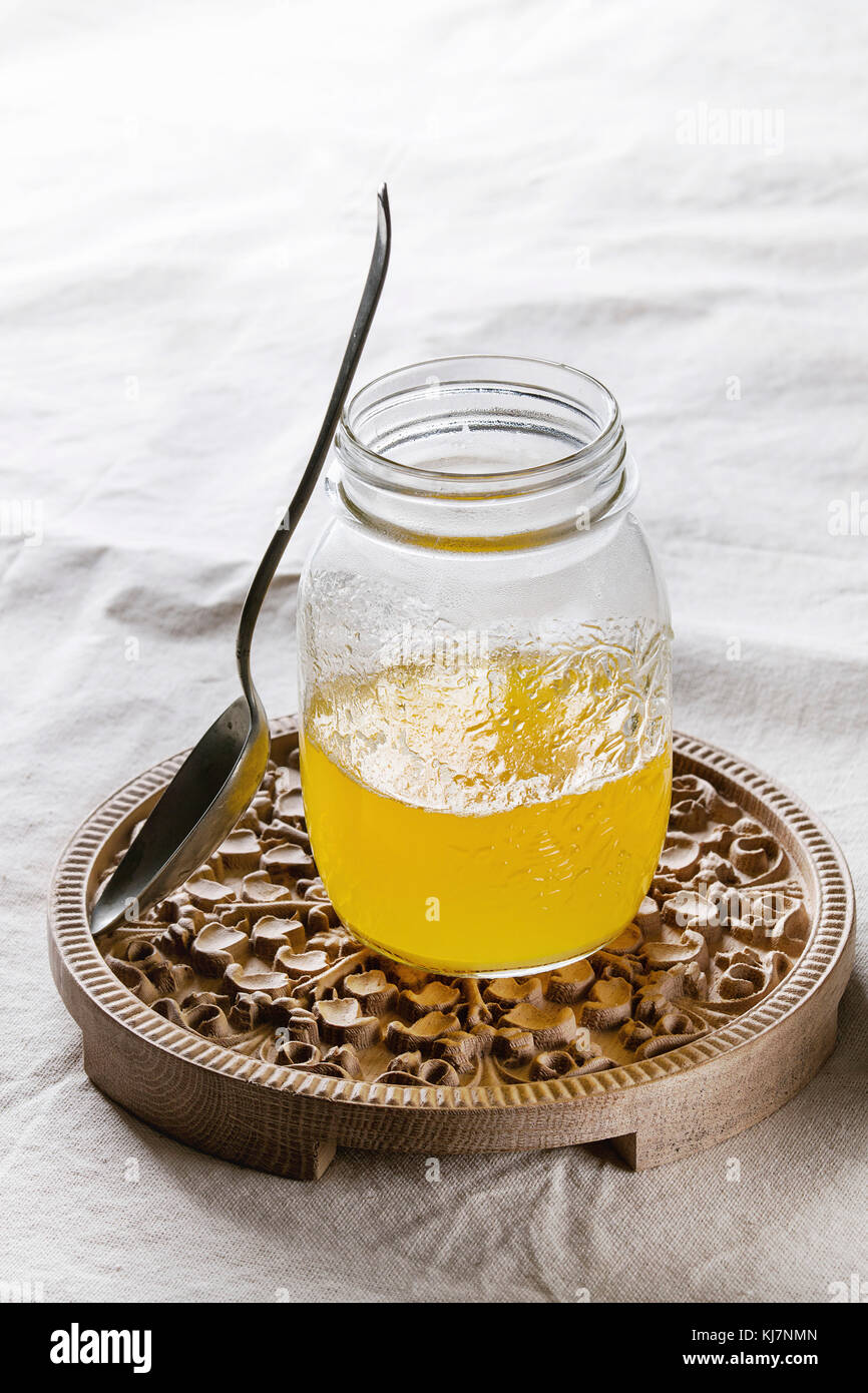 Glass of hot drawn ghee butter standing with spoon on wooden ornate