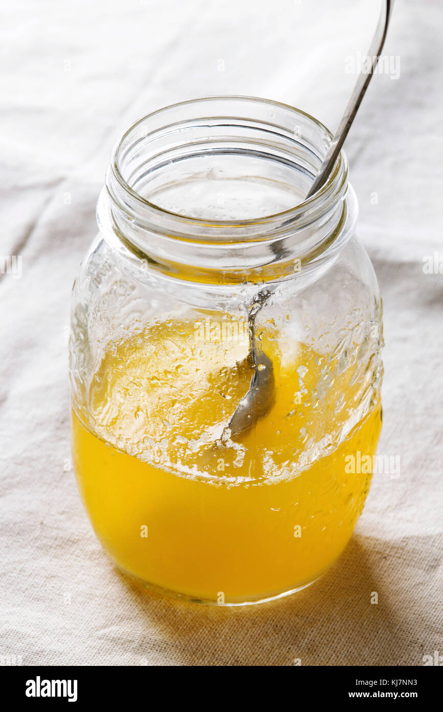 Glass of hot drawn ghee butter standing with spoon on wooden ornate