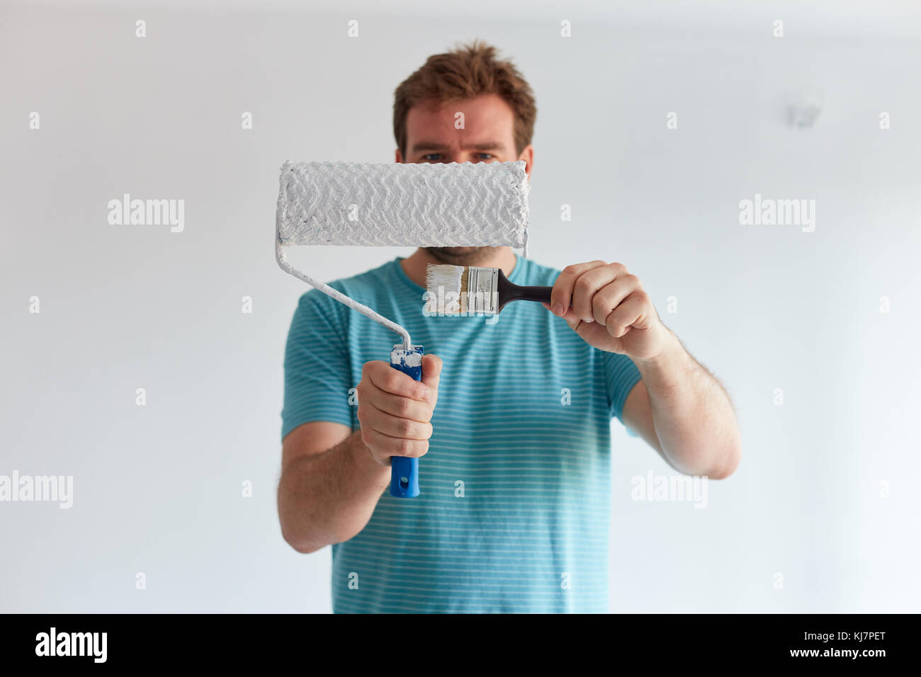 Smiling man holding a brush and a roller in front of him Stock Photo