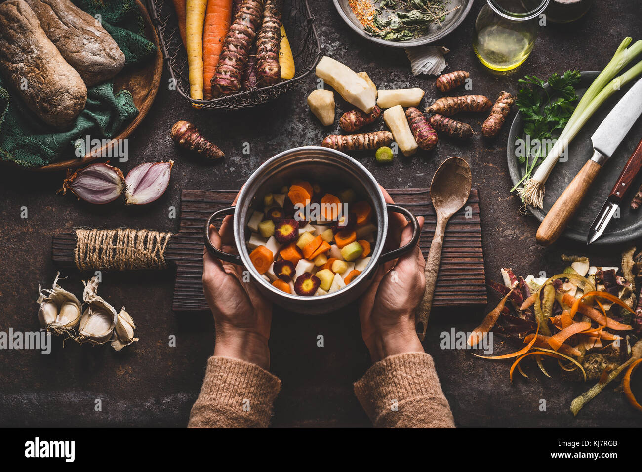 Female woman hands holding pan with diced colorful vegetables on dark rustic kitchen table with vegetarian cooking ingredients and tools. Healthy and  Stock Photo