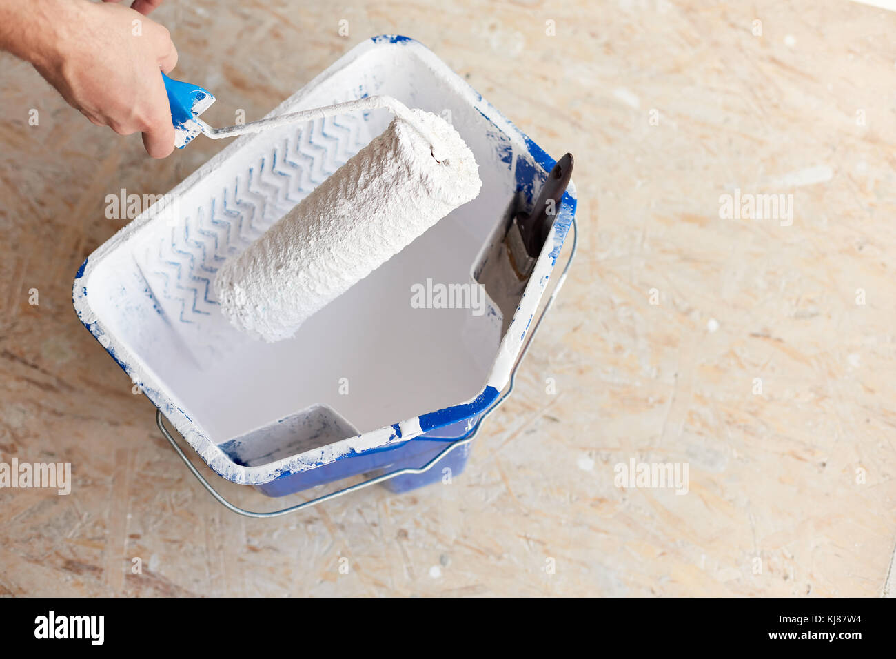 A bucket of white paint with a male hand holding a brush roller Stock Photo