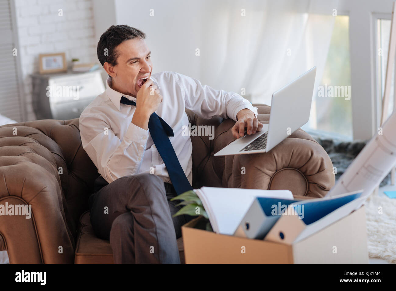 Tired working man feeling sleepy while sitting with a laptop Stock Photo