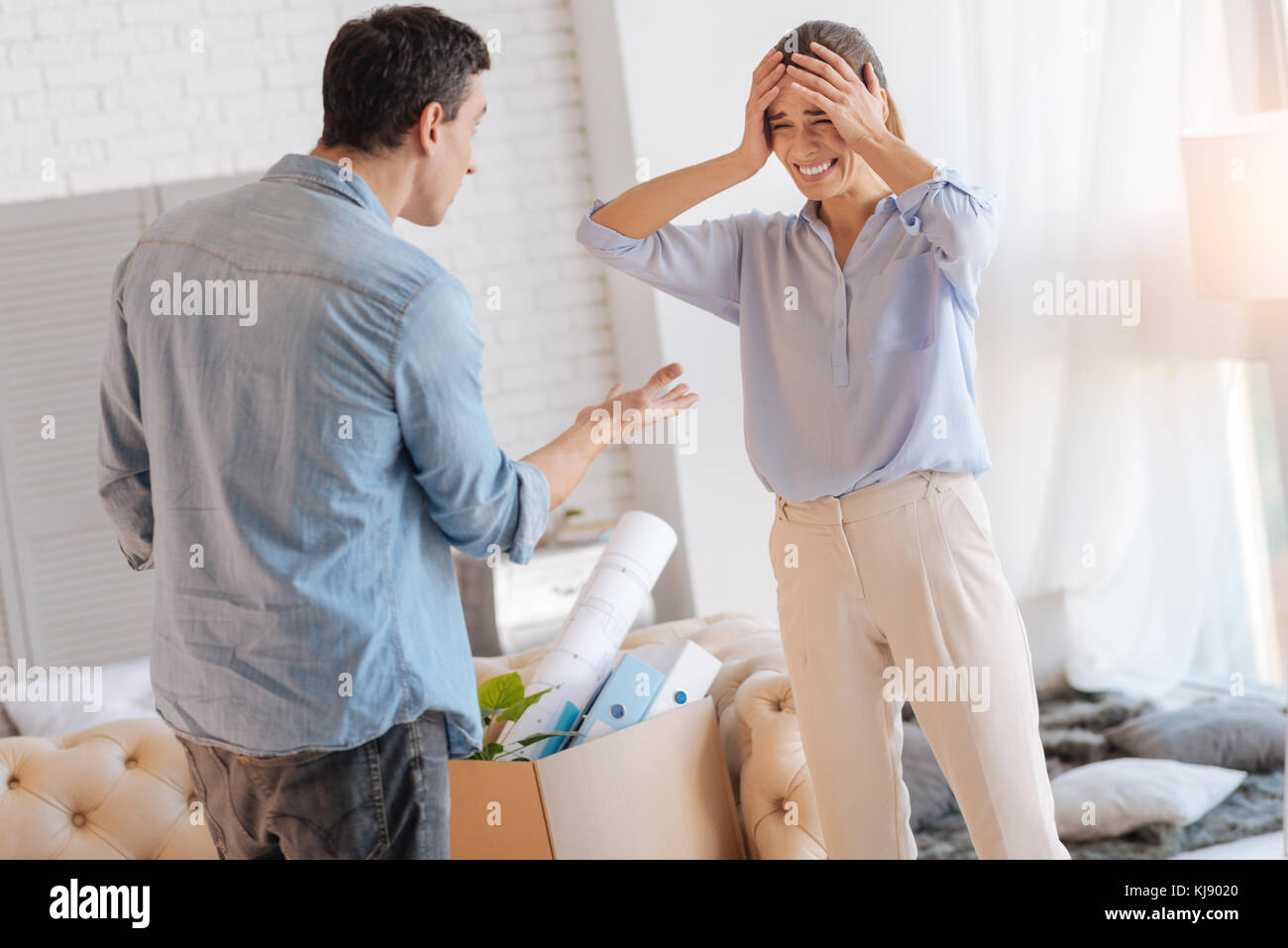 Emotional irritated woman touching her head while having a quarrel with husband Stock Photo