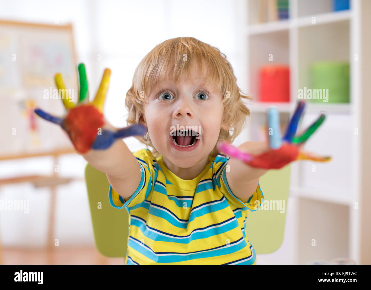 Child boy draws with hands and shows multi-colored painted palms. Children's educational games with paints. Stock Photo
