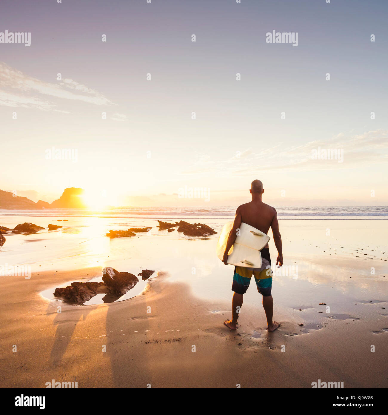 Silhouette Of A Surfer Man At The Beach With His Surfboard Stock Photo