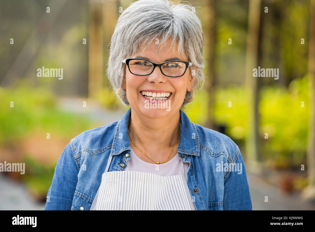 Beautiful mature woman working in a greenhouse, looking at camera and smiling Stock Photo