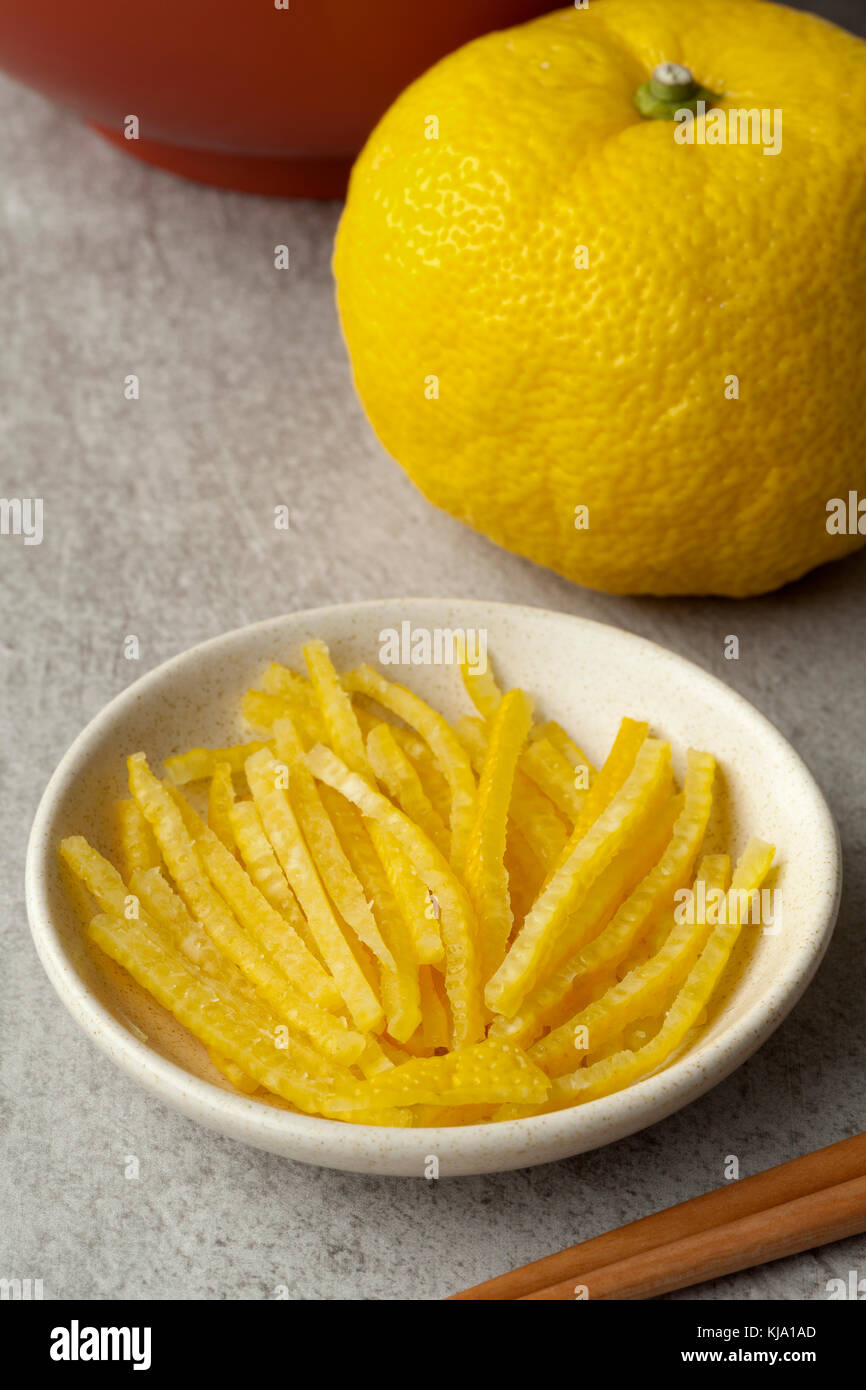 Fresh strips of a yellow Japanese Yuzu skin with a whole yuzu in the background Stock Photo