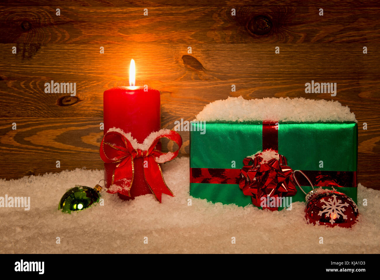 A gift wrapped Christmas present with candle and snow against a wooden background. Stock Photo