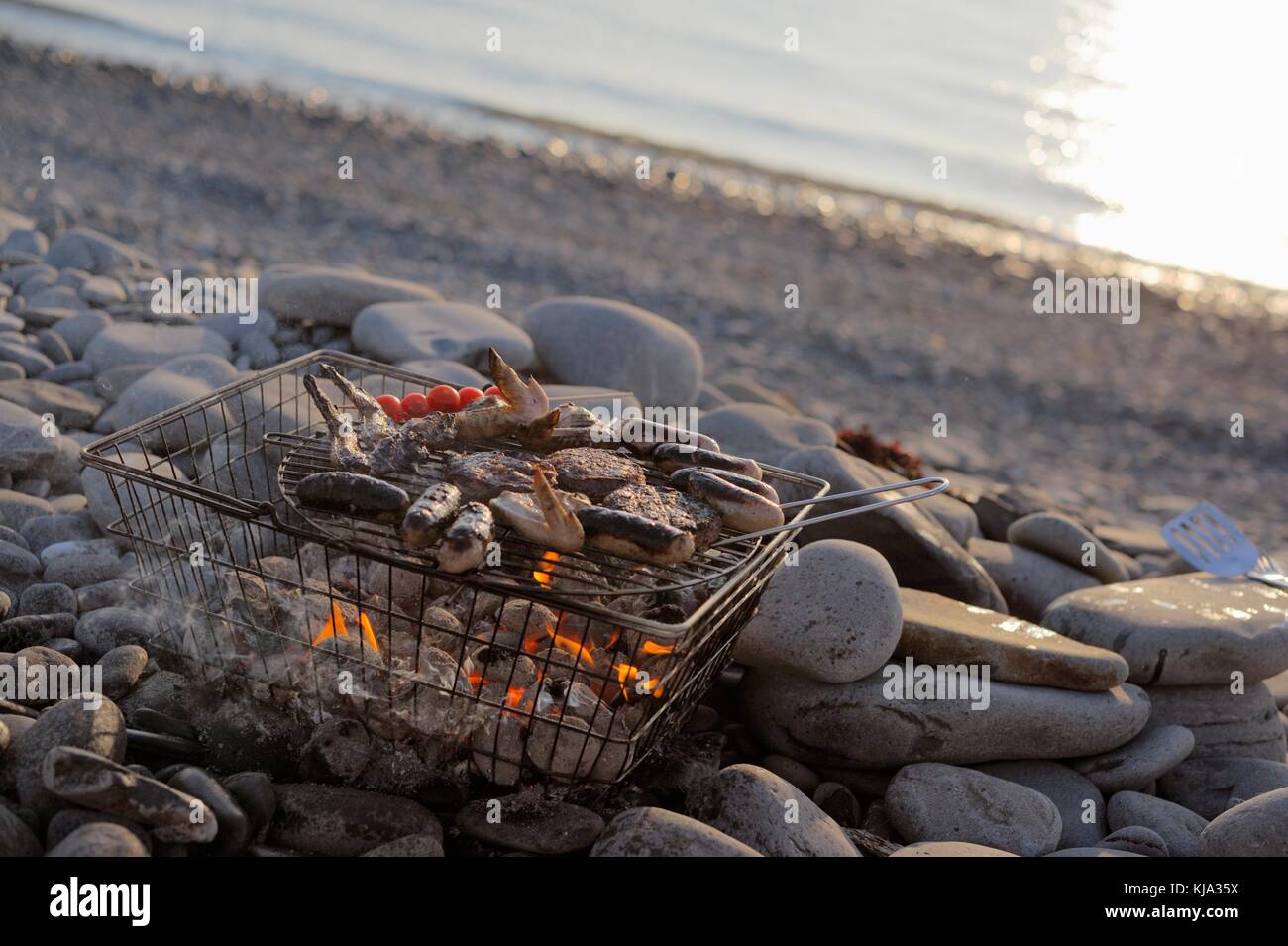 Sausages, burgers, chicken and tomatoes cooking on a barbecue in a
