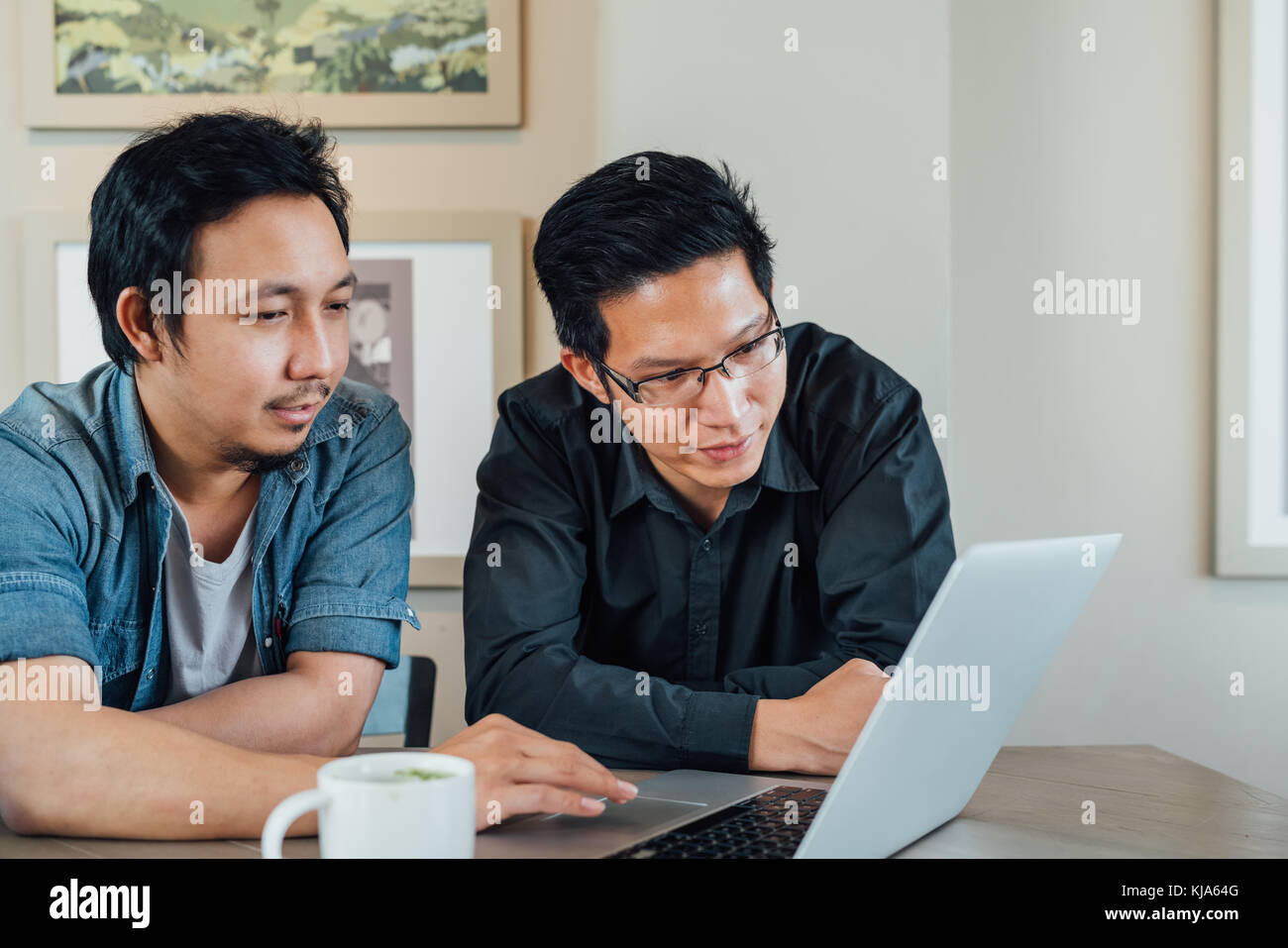 Two Asian businessman or business partner discussing project together using laptop computer at coffee shop. Casual team meeting, teamwork, or startup Stock Photo