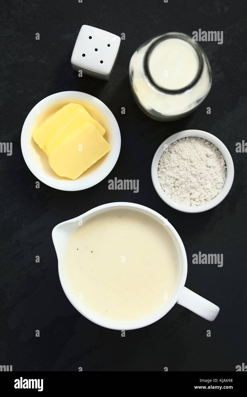 Homemade French Bechamel or White Sauce served in sauce boat with ingredients on the side (flour, butter, milk), photographed overhead on slate Stock Photo