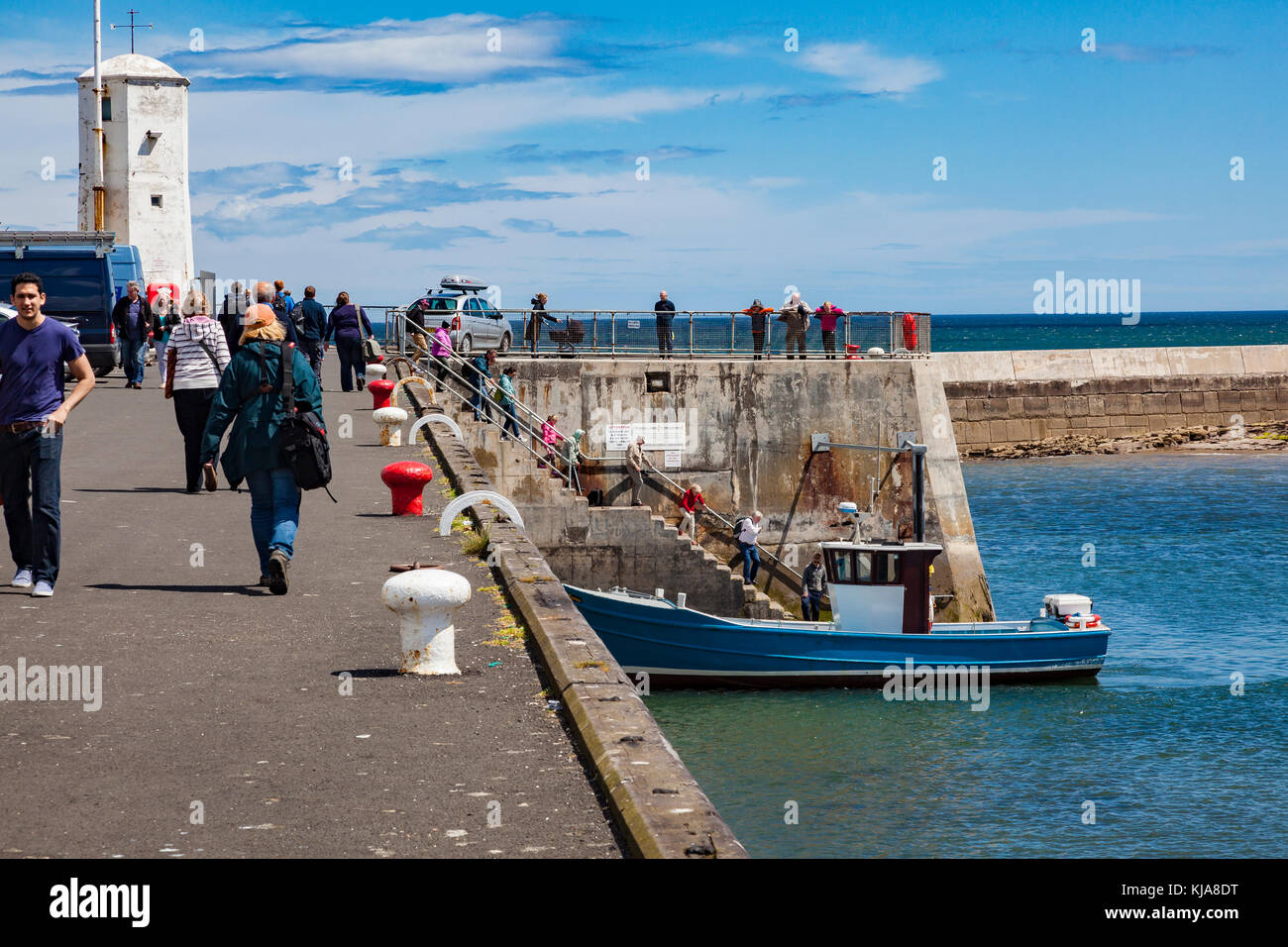 Summer crowds of visitors at Seahouses, queue down the harbour steps to catch boat trips to the Farne Islands, Northumberland, UK Stock Photo