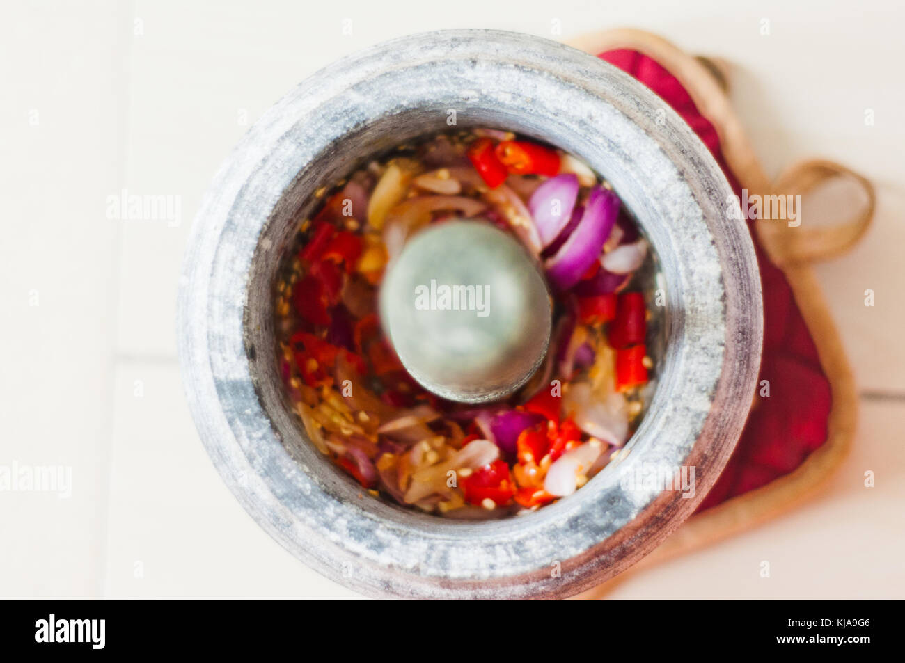 A mortar and pestle or lesung batu in Malay with crushed chilies, fried shallots and shrimp paste mixed together. Soft focus, shallow depth of field. Stock Photo