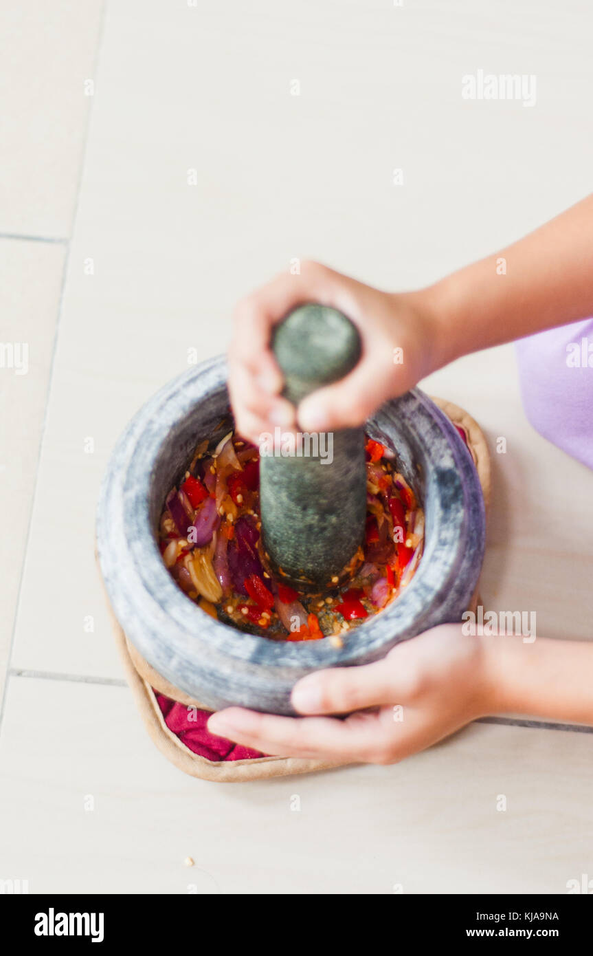 A mortar and pestle or lesung batu in Malay with crushed chilies, fried shallots and shrimp paste mixed together. Soft focus, shallow depth of field. Stock Photo