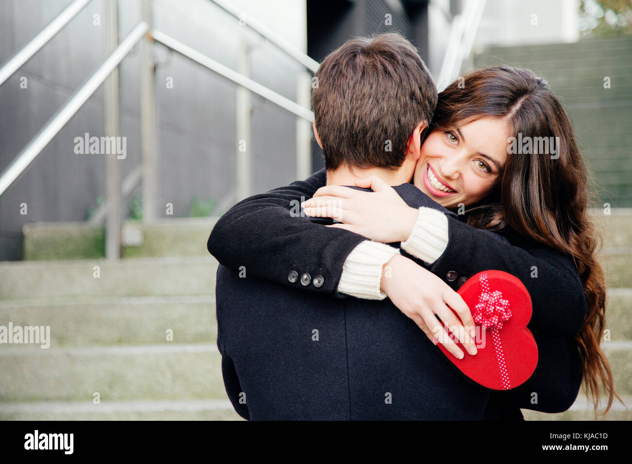 Beautiful and happy young woman in love hugging her boyfriend holding a ...