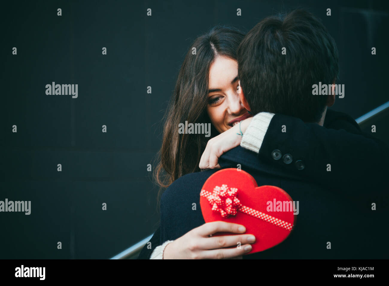 Beautiful and happy young woman in love hugging her boyfriend holding a ...