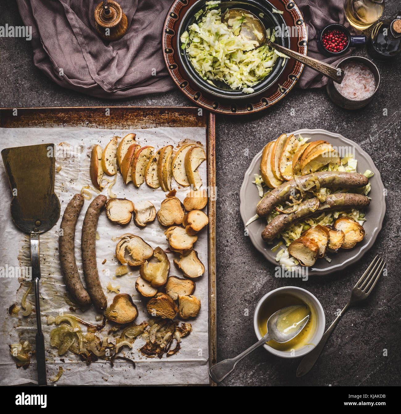 Fried sausages on baking tray served on plate with white coleslaw salad and mustard dip on rustic kitchen table, top view. German food concept. Stock Photo