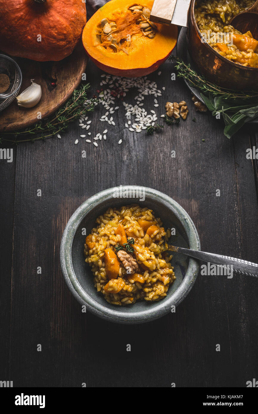 Bowl with vegetarian pumpkin risotto and spoon on dark rustic kitchen table background with cooking ingredients, top view. Healthy clean seasonal food Stock Photo