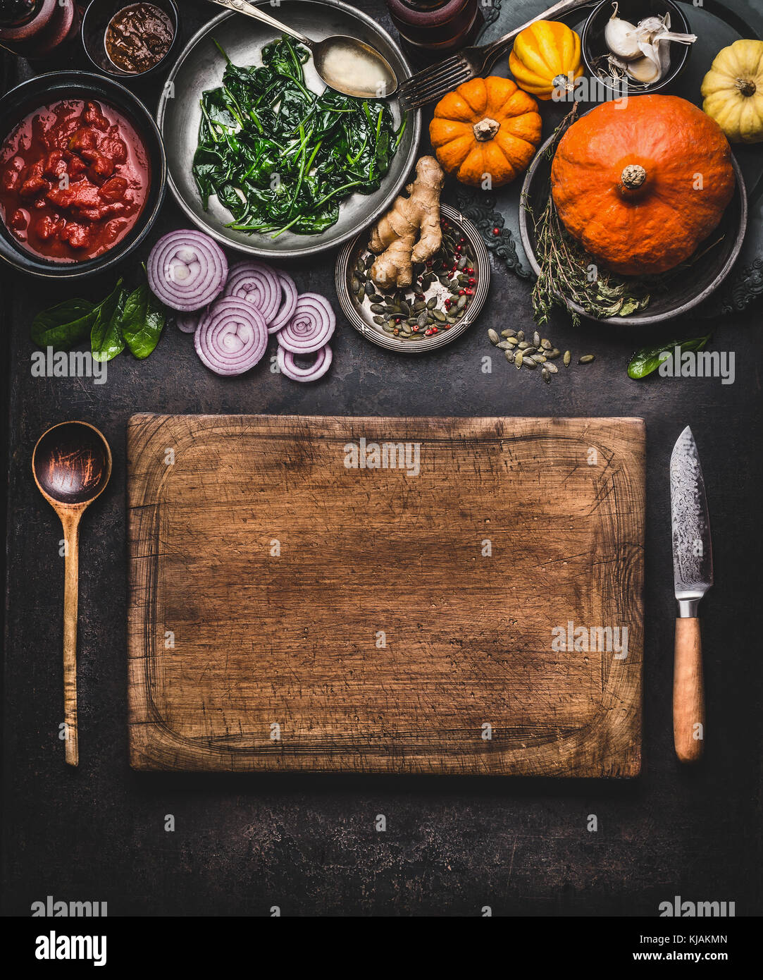 Pumpkin dish cooking. Food background with wooden cutting board, kitchen knife and spoon. Various vegetarian seasonal ingredients for tasty meal Stock Photo