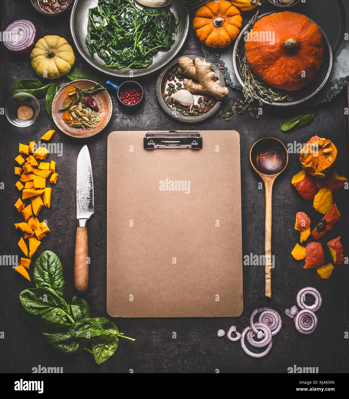Food background for tasty winter and autumn dishes with pumpkin. Various cooking ingredients with spoon and knife around blank cardboard clipboard Stock Photo