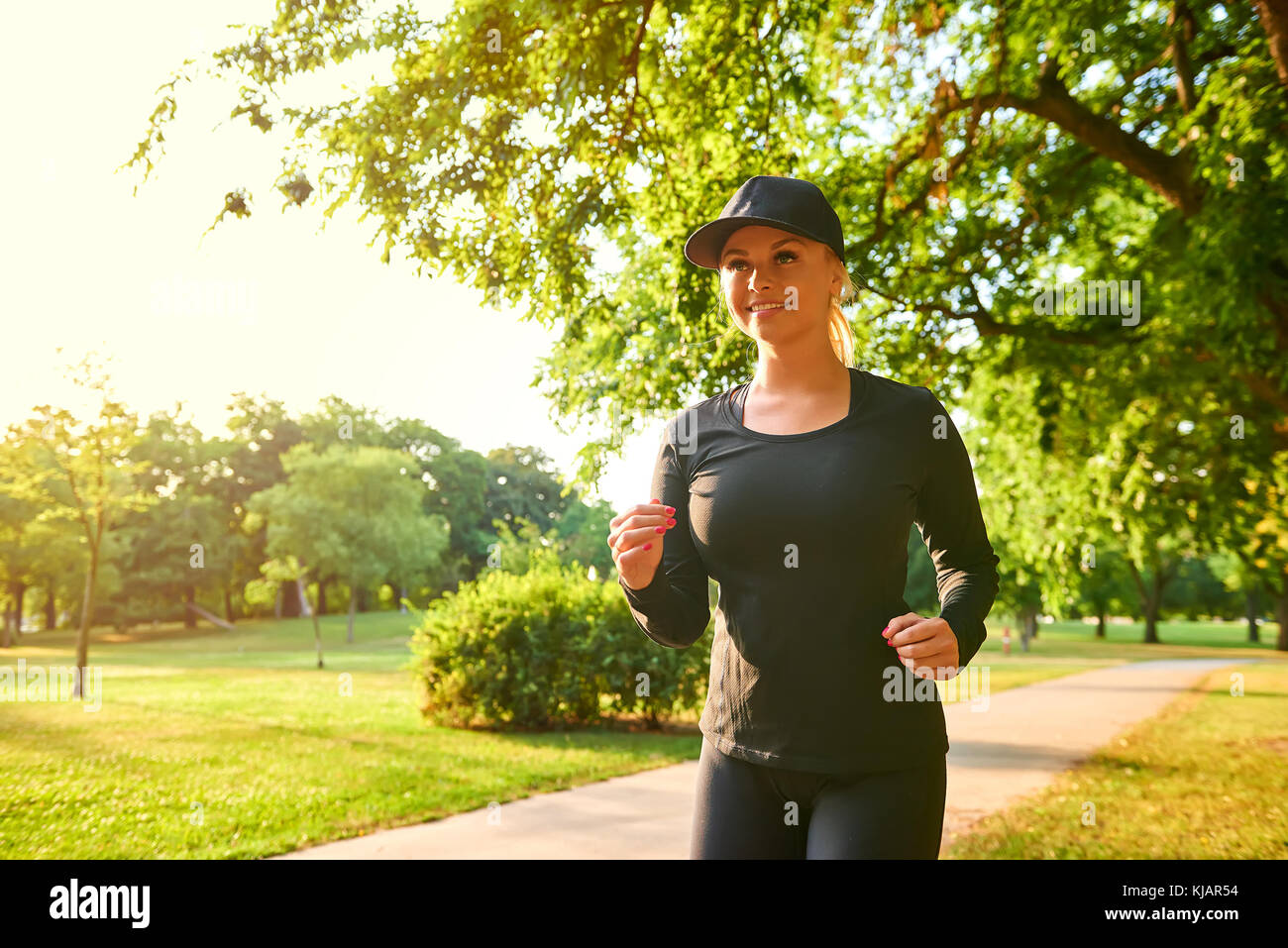 A beautiful young blonde woman wearing black clothes and baseball cap while  running in a park in the sunset Stock Photo - Alamy